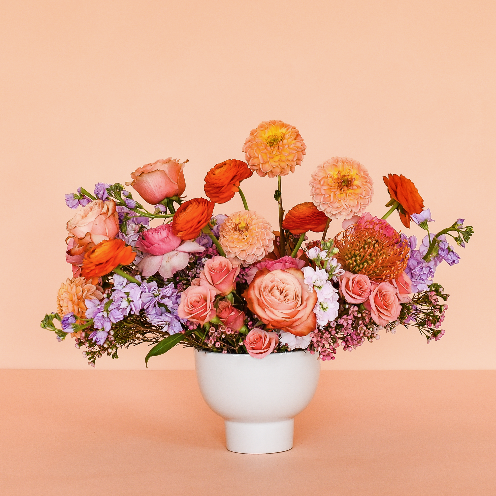 Assorted lush flowers with no greens in a low white vase