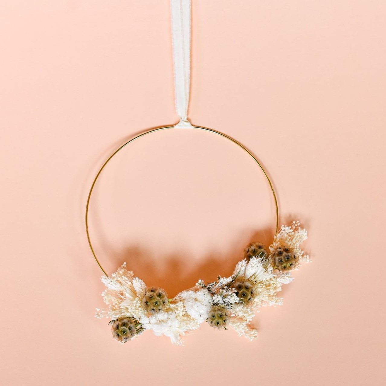 A gold frame wreath with dried white flowers and tan dried flower pods