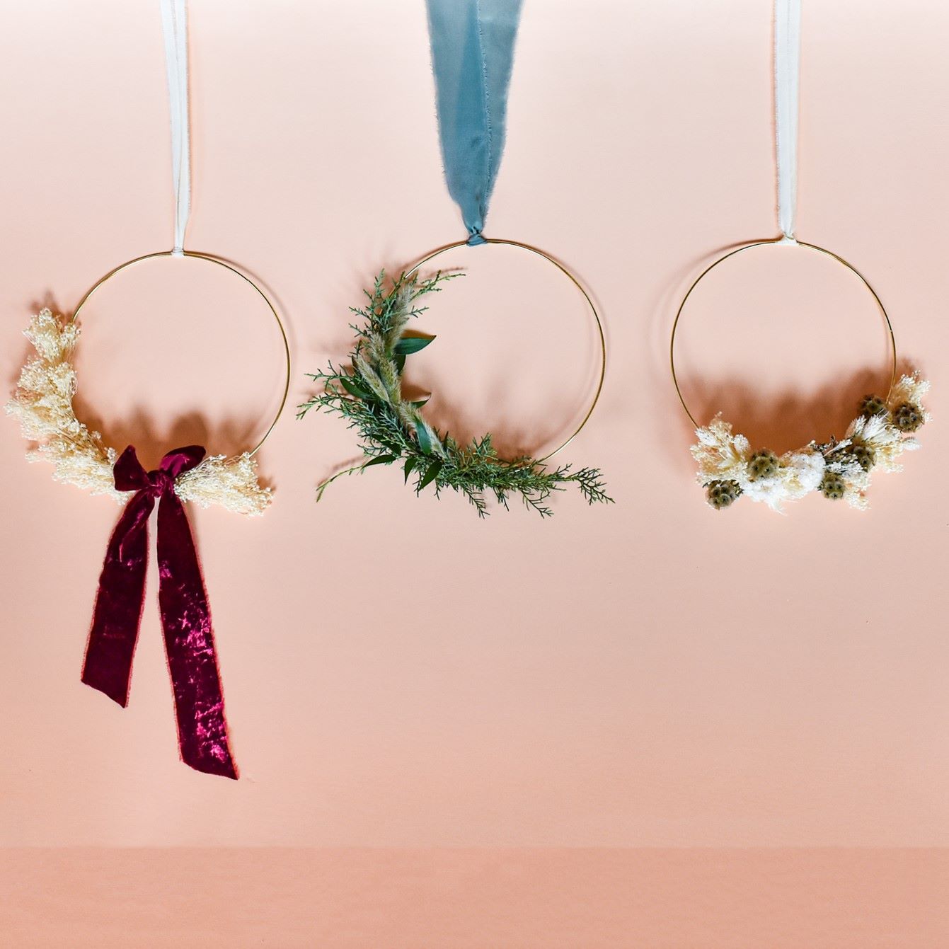 an arrangement of 3 different wreaths on gold frames with different colored dried flowers and ribbon