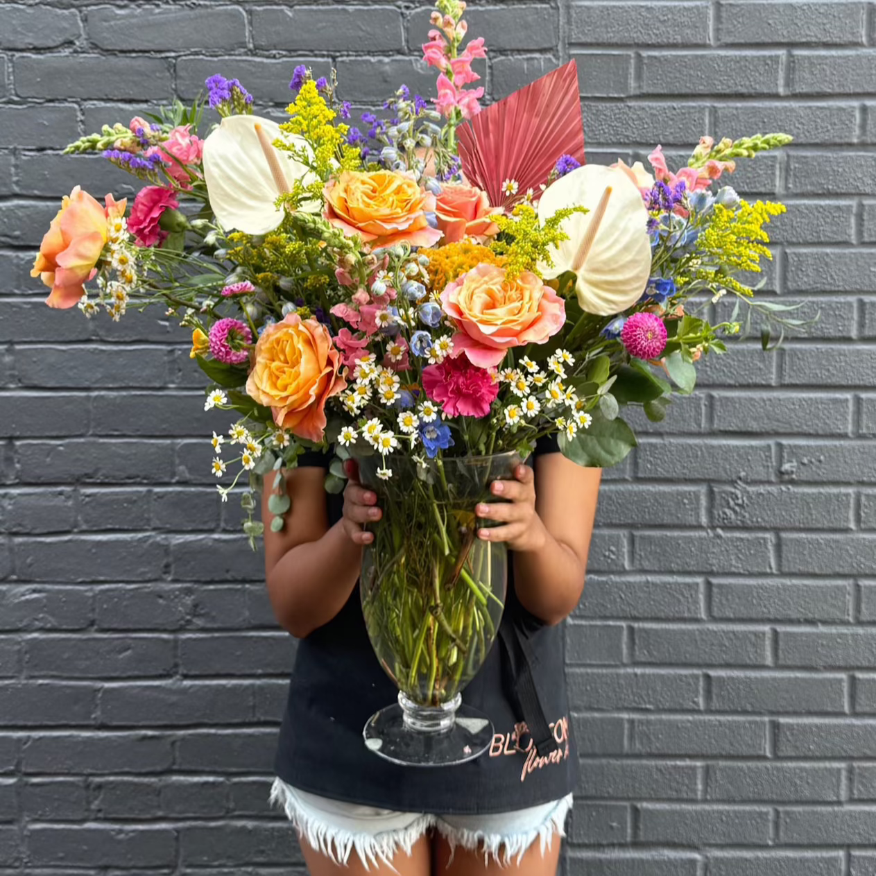 A woman holding a huge vase exploding with colorful flowers in a very large-scale arrangement